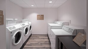 A laundry facility with multiple washing machines and dryers, a complimentary basket, and a sign indicating free guest laundry. - Candlewood Suites Baltimore - Inner Harbor by IHG (Baltimore)
