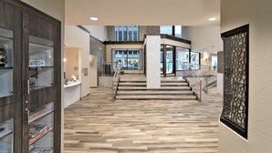 A hotel lobby with a wooden floor, a reception desk, and a staircase leading to an upper level.