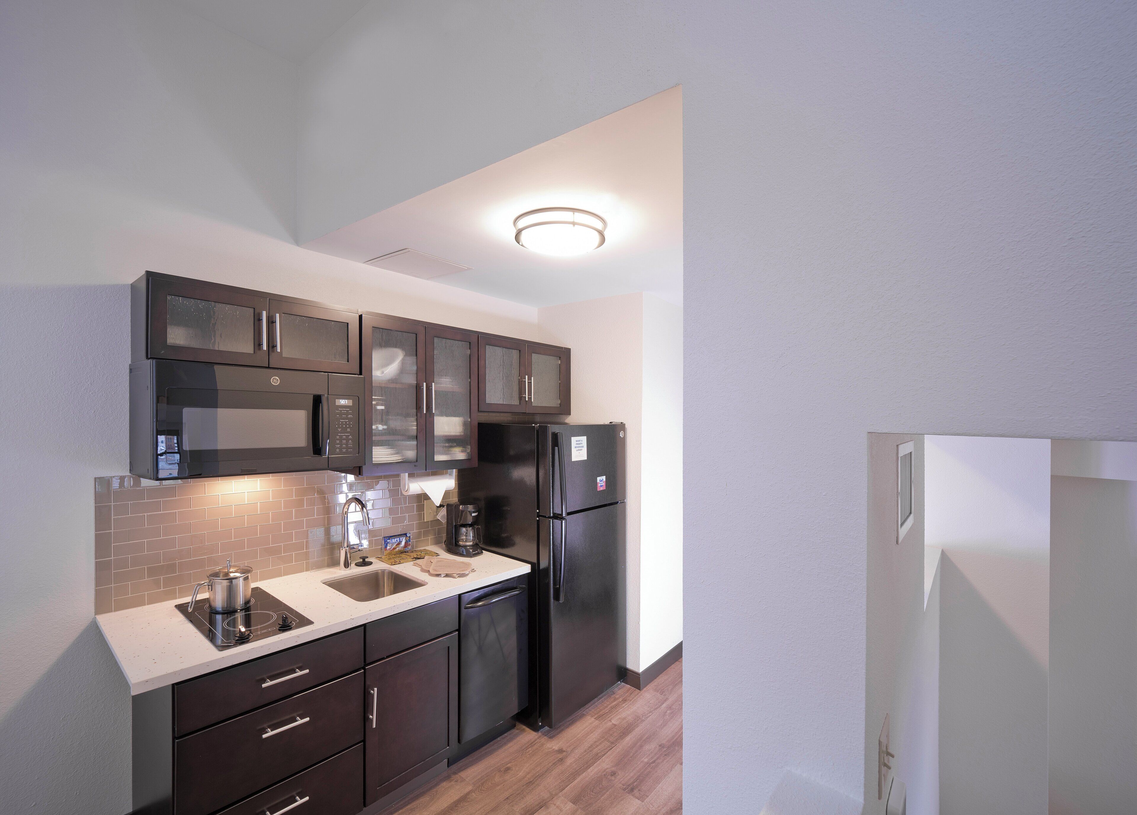 A compact kitchen with dark cabinets, a stainless steel refrigerator, and a built-in microwave.