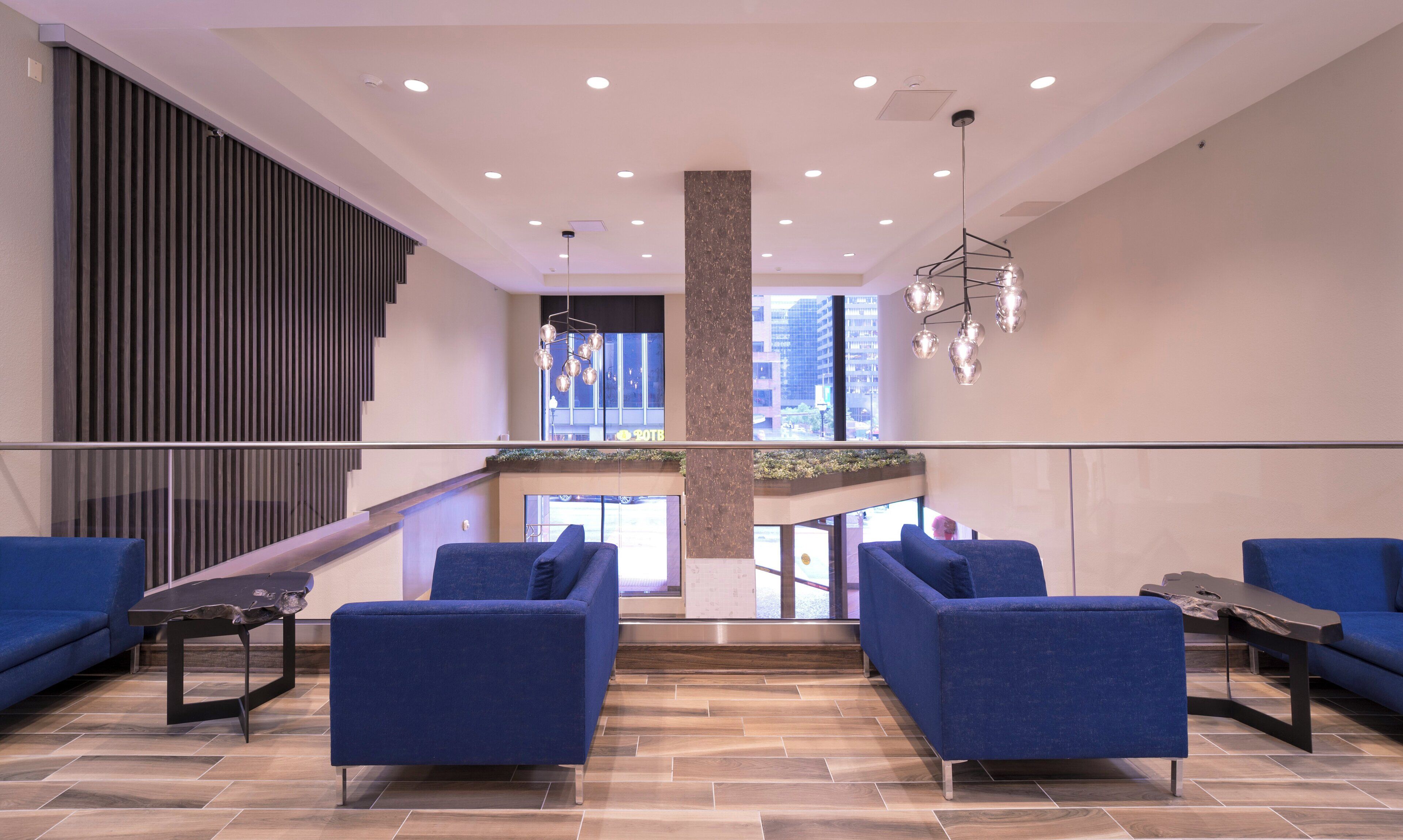 A modern lobby with a staircase, blue seating, and a chandelier.