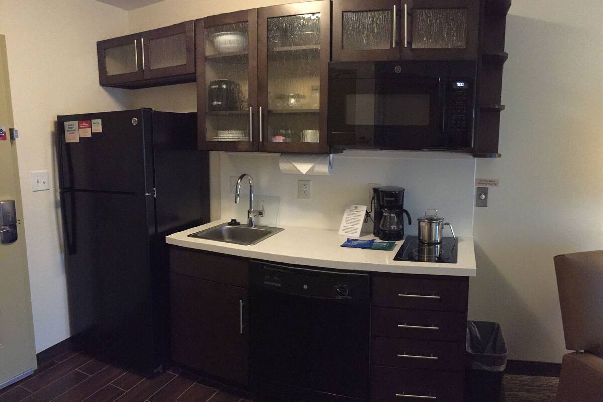 A compact kitchen with dark cabinetry, a stainless steel sink, a black refrigerator, a microwave, and a coffee maker.