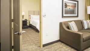 Una habitación de hotel con una cama, un sofá marrón, un cuadro en la pared y suelo alfombrado.