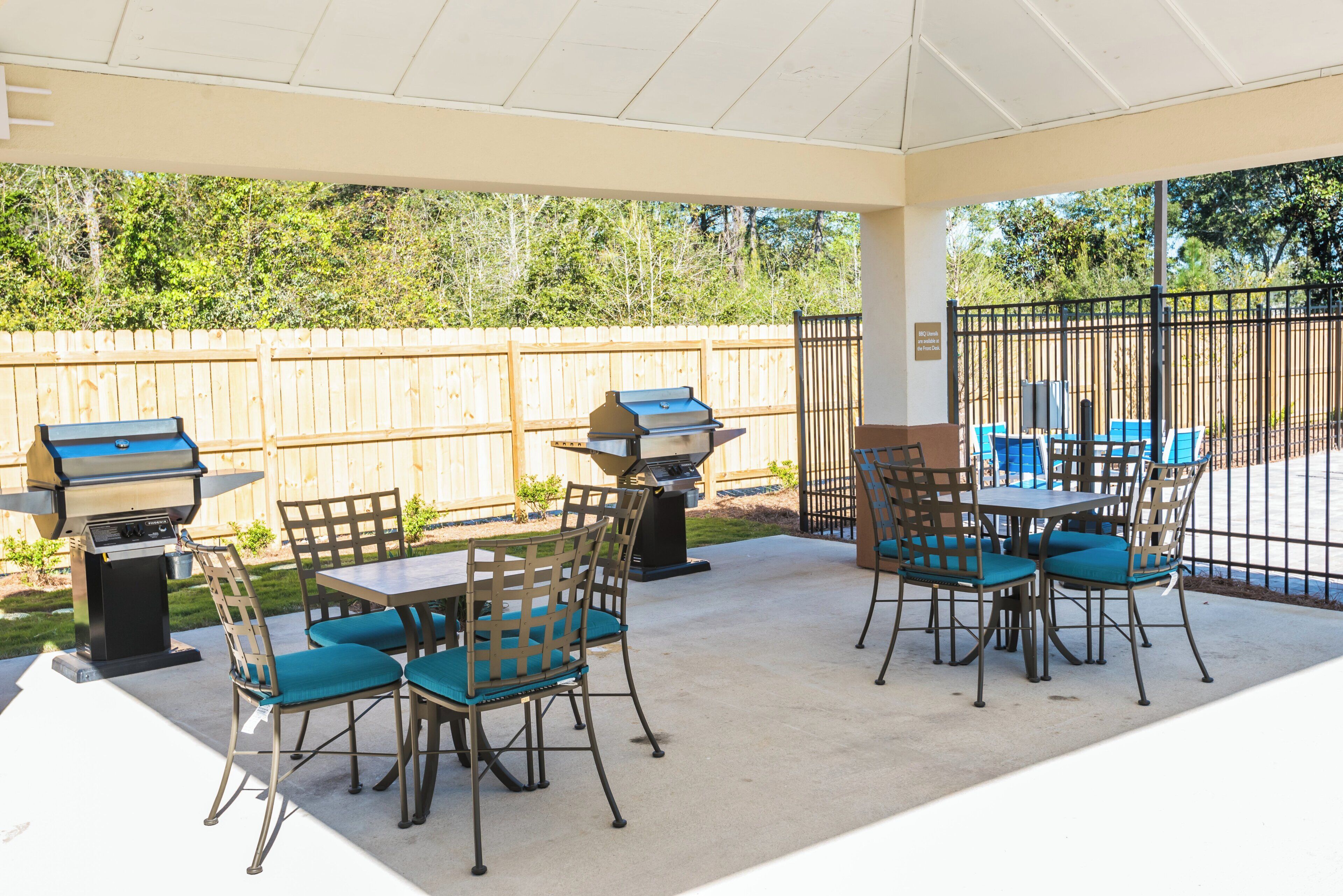 An outdoor patio with a covered seating area, two barbecue grills, and a fenced backyard.