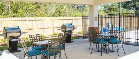 Une terrasse extérieure dotée d’un espace salon couvert, de deux barbecues et d’une cour arrière clôturée.