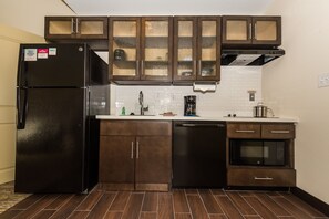 A kitchen with dark wooden cabinets, a black refrigerator, a dishwasher, a microwave, and a coffee maker. - Candlewood Suites Ft Walton Bch - Hurlburt Area by IHG (Fort Walton Beach)