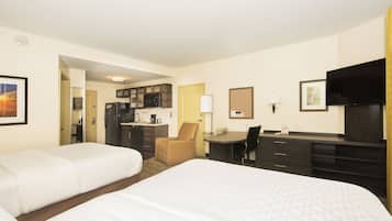 A hotel room with two beds, a desk, a chair, a kitchenette, and a TV.