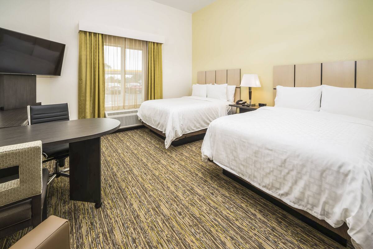 A hotel room with two beds, a desk, a chair, a TV, and a window with curtains.