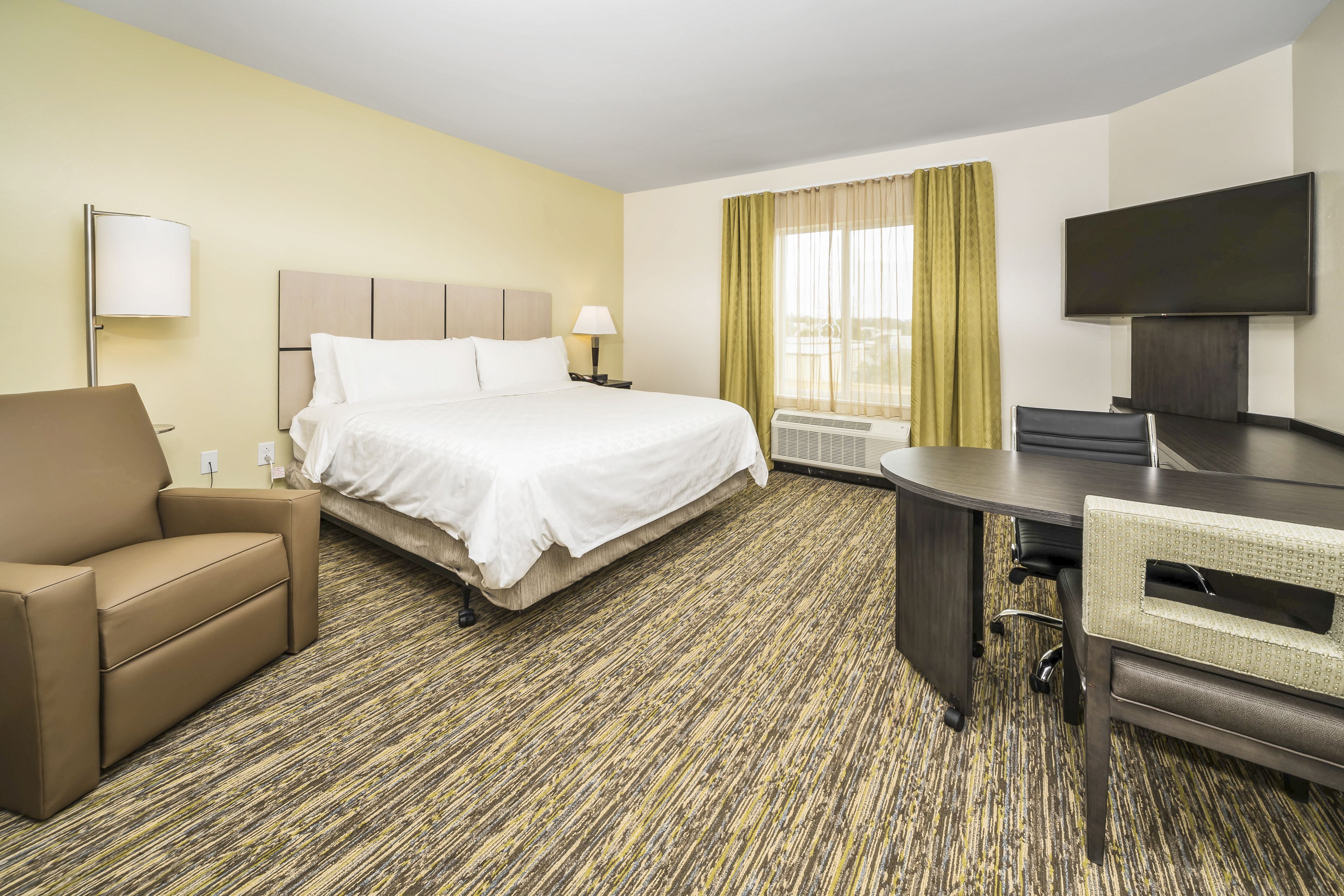 Une chambre d’hôtel avec un lit, un bureau, une chaise, une télévision et une fenêtre avec des rideaux.
