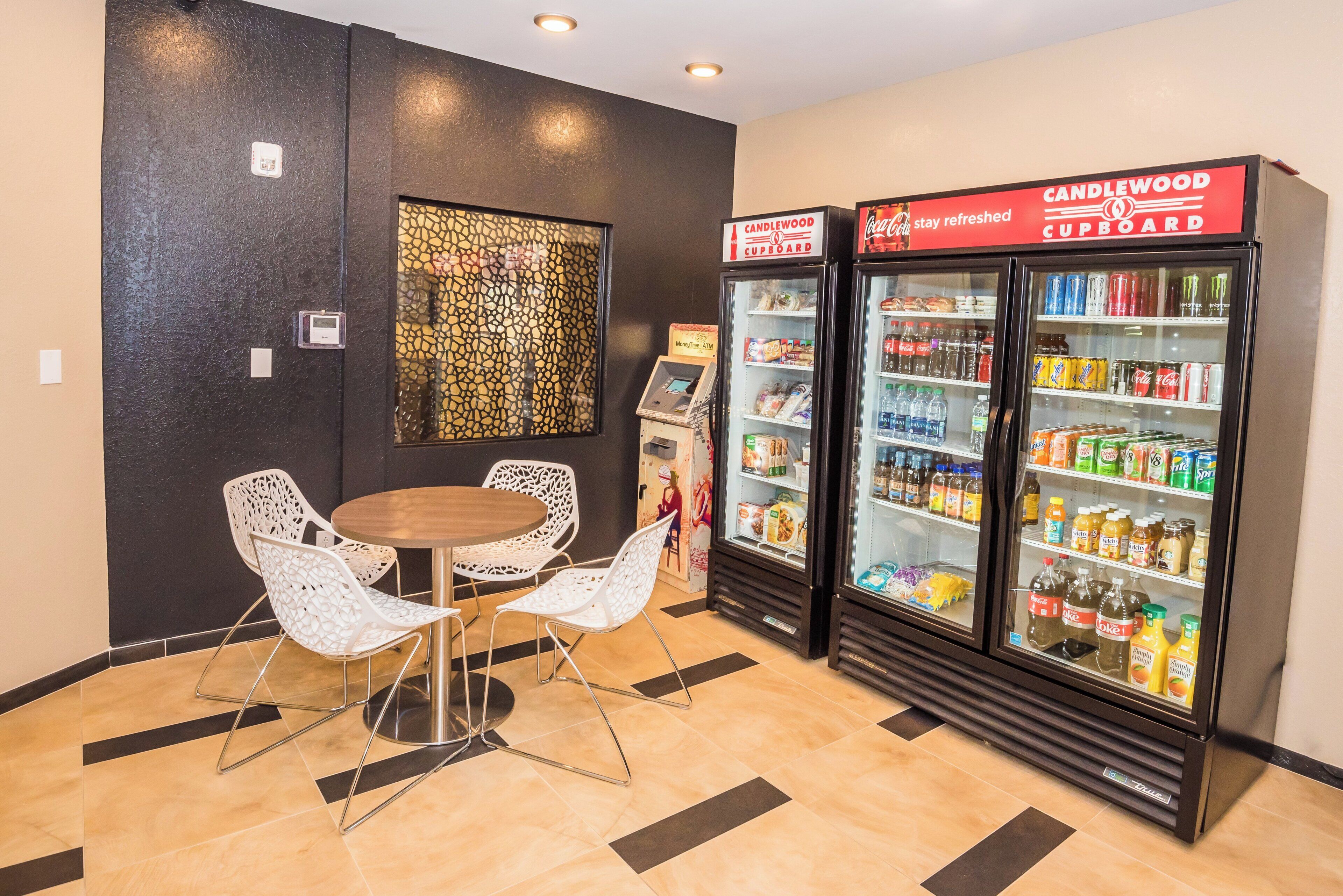 A room with a table and chairs, a refrigerator stocked with beverages, and a wall-mounted ATM.