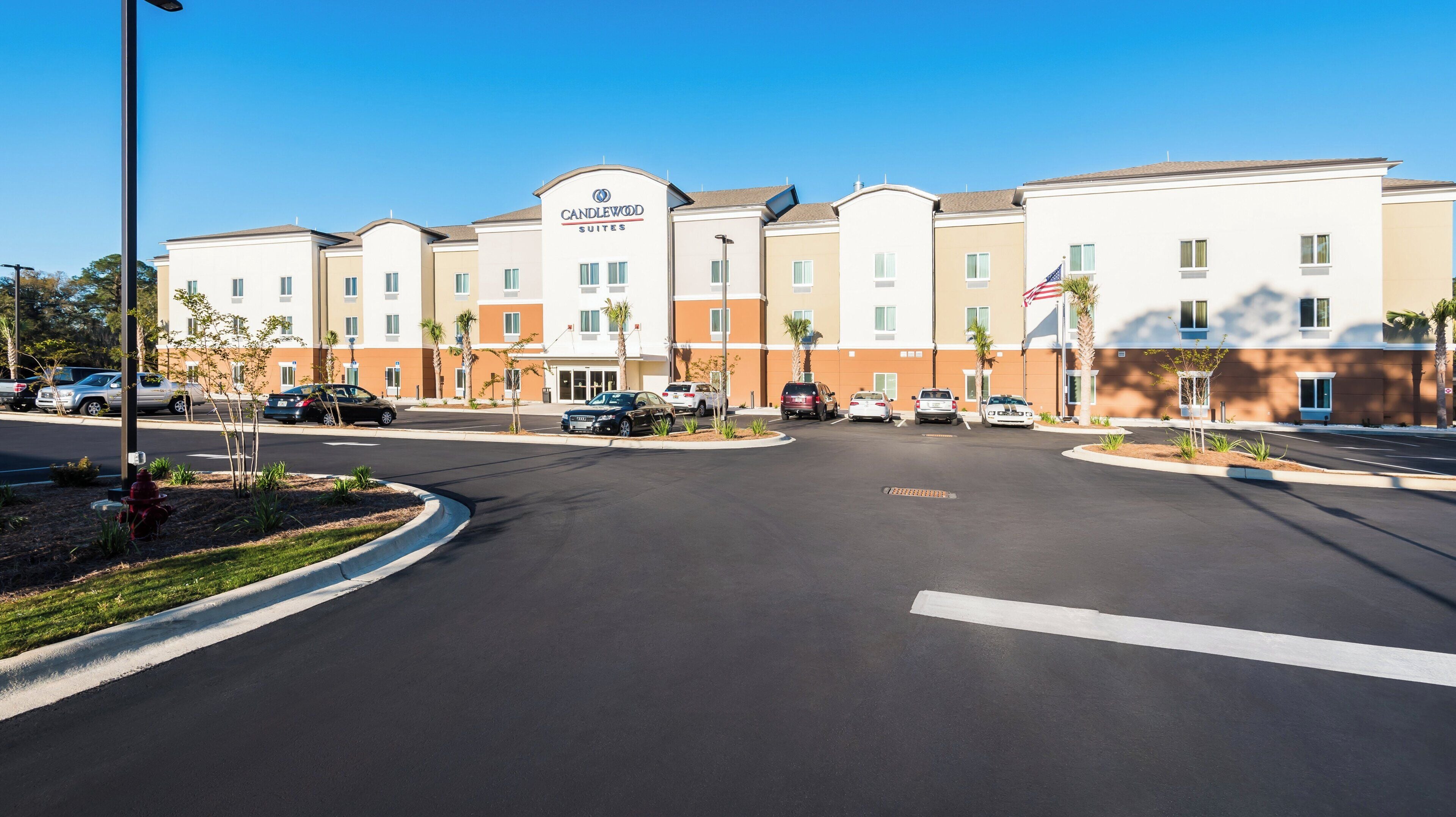 A multi-story hotel with a central courtyard, parking lot, and a flagpole with an American flag.