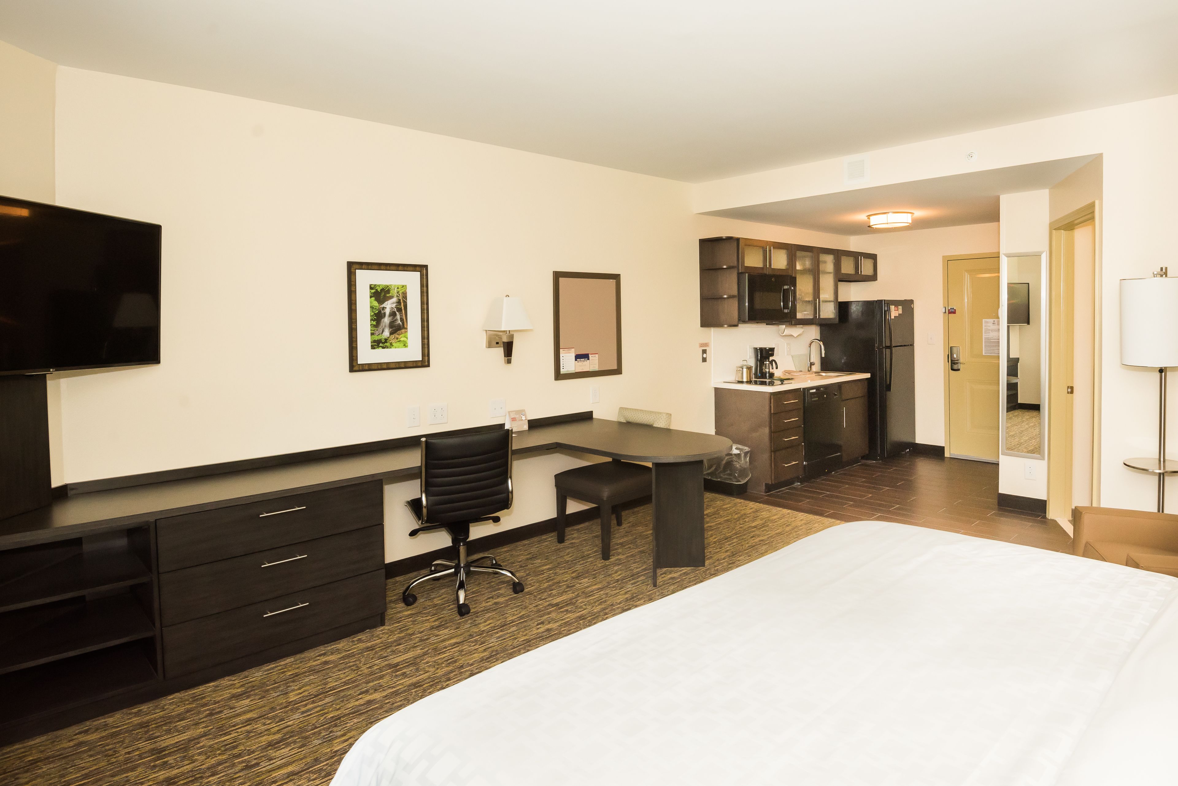 A hotel room with a bed, a desk, a chair, a television, a kitchenette, and a bathroom.
