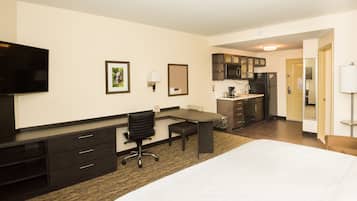 A hotel room with a bed, a desk, a chair, a television, a kitchenette, and a bathroom.