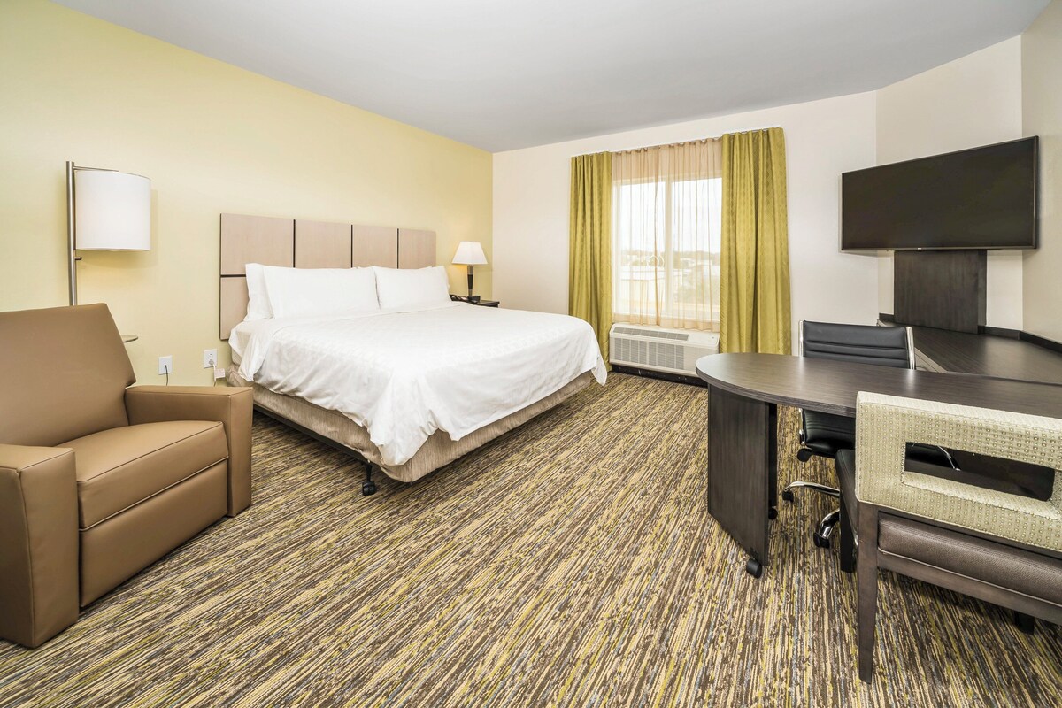 Habitación de hotel con cama, escritorio, silla, televisor y ventana con cortinas.