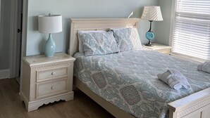 Quarto com cama, mesas de cabeceira, ventilador de teto e janela com persianas.