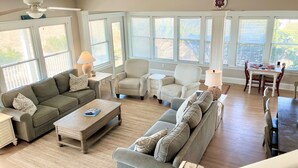 Uma sala de estar espaçosa com um amplo sofá modular cinza, uma mesa de centro de madeira e um espaço de jantar com mesa e cadeiras.