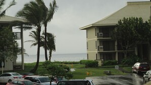 A hotel with a view of the ocean, a parking lot with several cars, and palm trees.