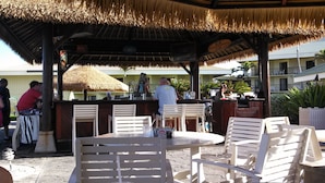 An outdoor bar area with a thatched roof, wooden chairs, and tables.