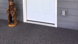 A white door with a glass panel and a wreath, a wooden bear sculpture, and a wall-mounted light fixture.