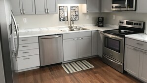 A modern kitchen with stainless steel appliances, grey cabinetry, and a marble countertop.