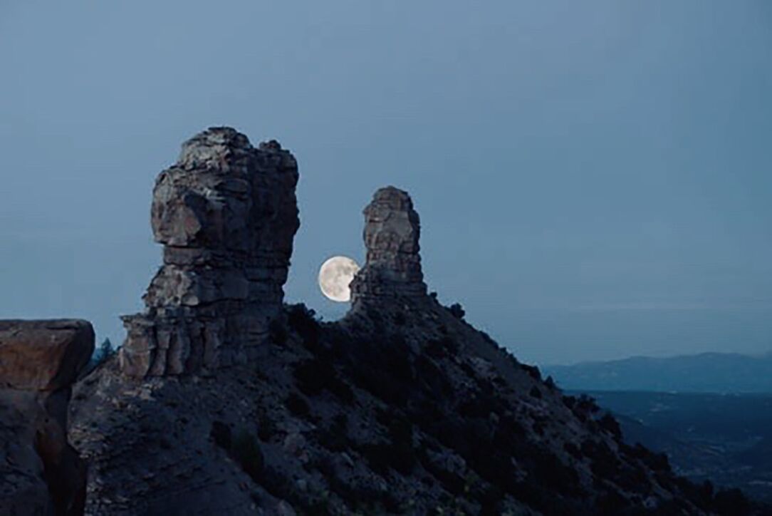 Une formation rocheuse illuminée par la lumière de la lune, offrant une vue dégagée sur la lune et les montagnes lointaines.