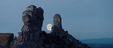 Une formation rocheuse illuminée par la lumière de la lune, offrant une vue dégagée sur la lune et les montagnes lointaines.