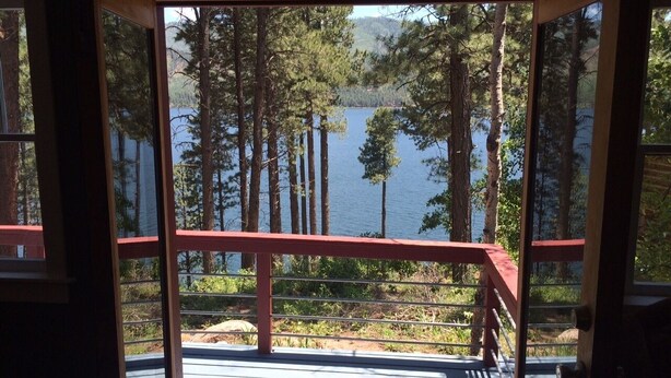 A wooden deck with a red railing overlooking a lake surrounded by trees.