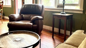 A living room with a brown leather chair, a round table, and a lamp near a window.