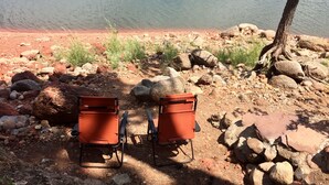 Two orange chairs with black frames placed on a rocky terrain near a body of water.