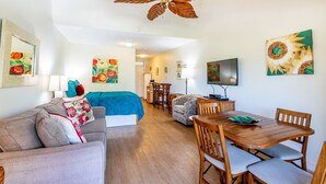 Een kamer met een bed, een bank, een eettafel met stoelen, een plafondventilator en kunstwerken aan de wanden.