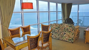 A room with a dining table, chairs, a sofa, and a large window with a view of the ocean. - Oceanfront  Seaside Resort 1403 3BR/3BA. Resort Amenities with Amazing views (NO. MYRTLE BEACH)