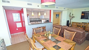 A dining area with a glass-top table, woven placemats, wicker chairs, and a brown leather sofa. - Oceanfront  Seaside Resort 1403 3BR/3BA. Resort Amenities with Amazing views (NO. MYRTLE BEACH)