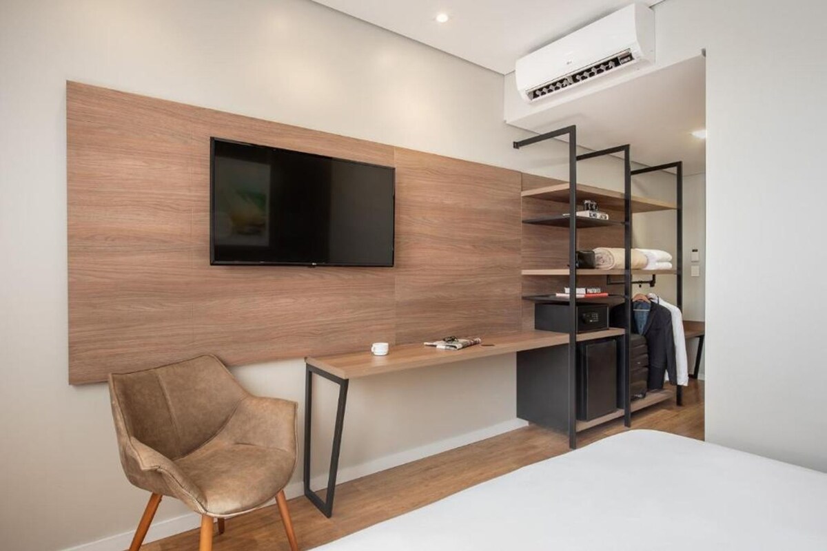 Une chambre moderne dotée d’un téléviseur fixé au mur, d’un panneau mural en bois, d’un bureau avec une chaise et d’une armoire intégrée avec des étagères.