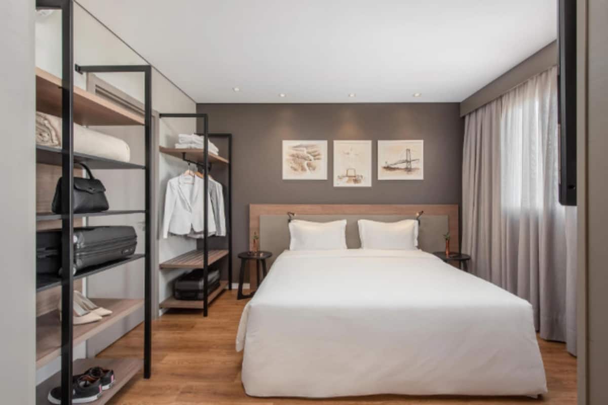 Ein modernes Hotelzimmer mit einem großen Bett, einem Kleiderschrank mit Ablageflächen und einem Kunstwerk an der Wand.