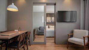 Ein modernes Wohnzimmer mit einem Holzes Esstisch, Stühlen, einer Couch und einem an der Wand befestigten Fernseher.