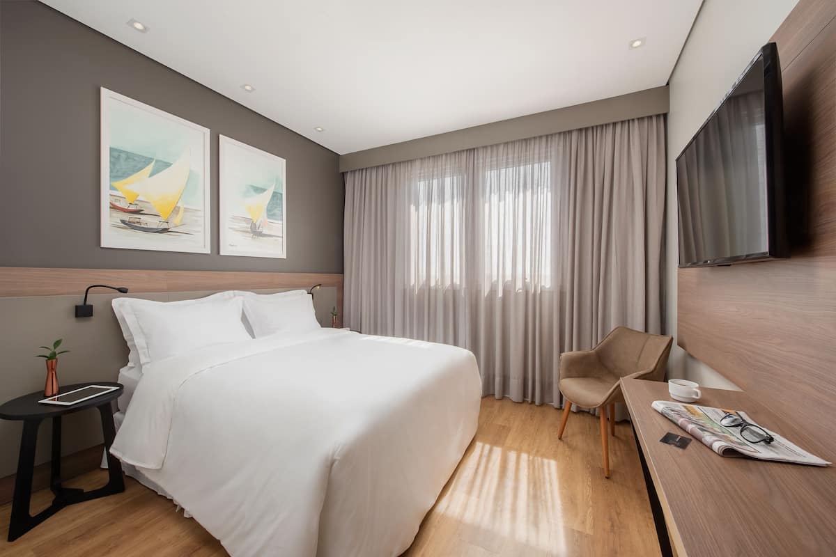 Ein modernes Hotelzimmer mit einem großen Bett, einem Schreibtisch mit Stuhl, einem Flachbildfernseher und Kunstwerken an der Wand.