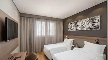 A hotel room with two beds, a desk with a chair, a TV, and a large abstract painting on the wall.