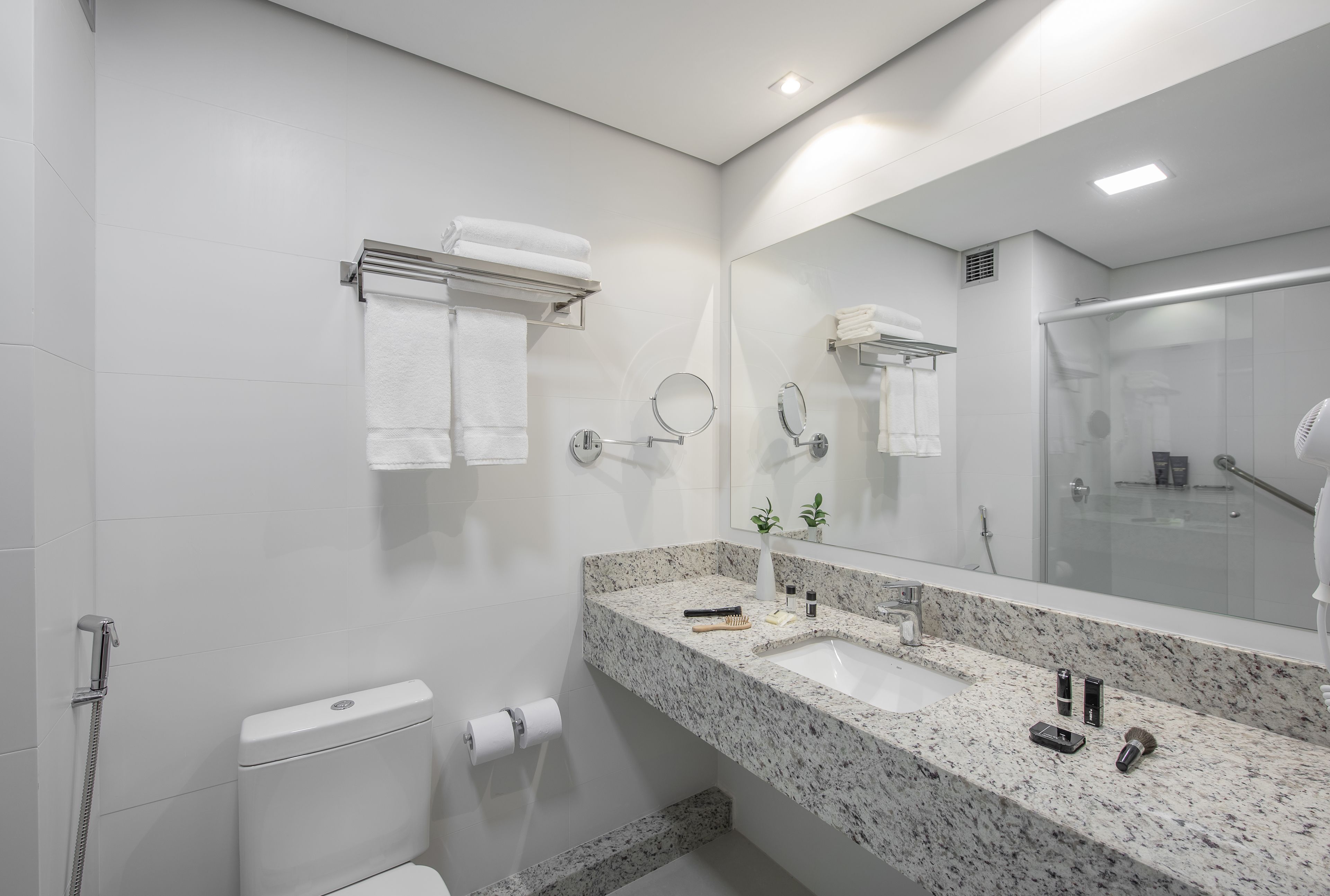 Un baño moderno con lavamanos de mármol, dos espejos, un perchero y una zona de ducha.