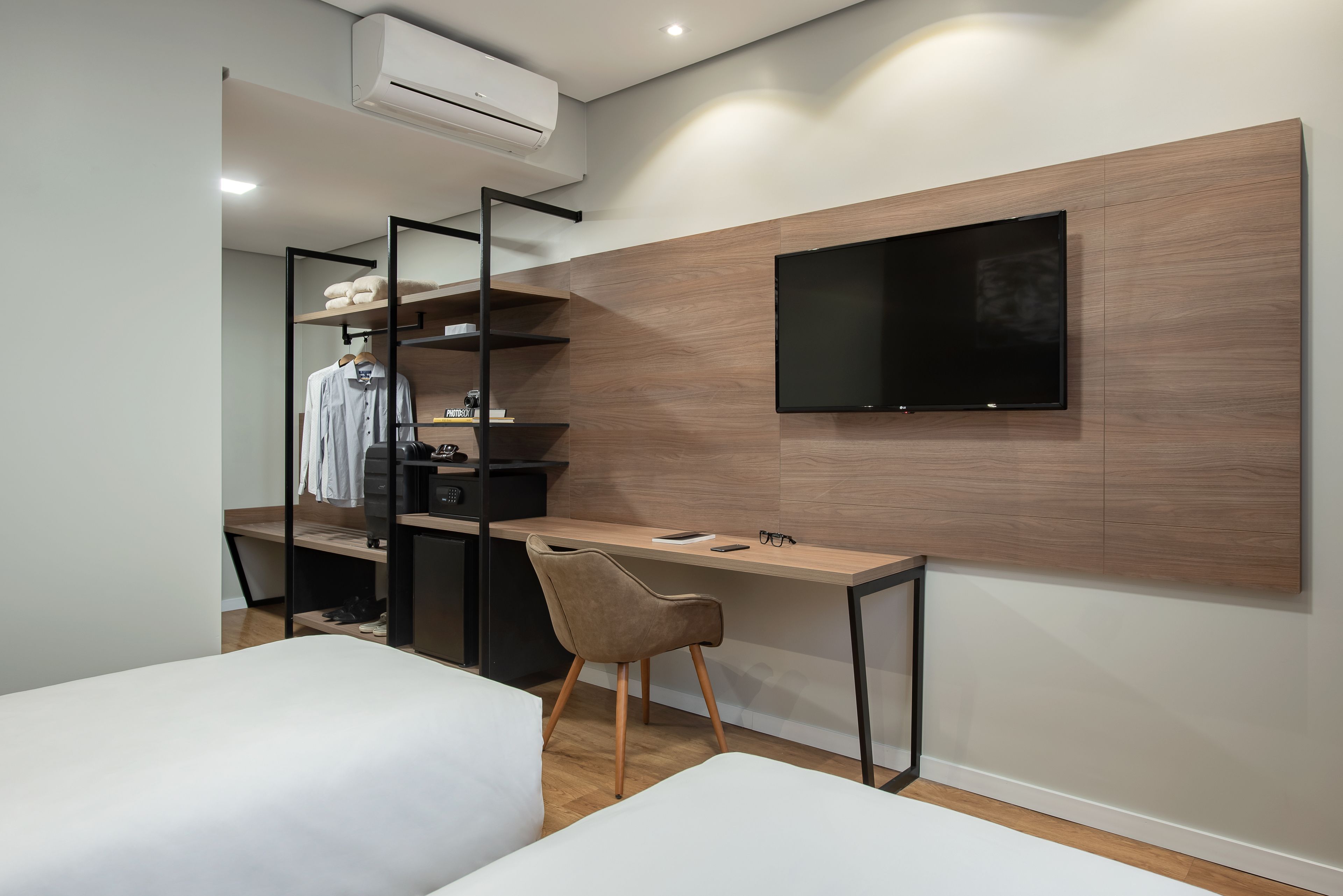 A modern bedroom with a bed, a desk, a chair, and a TV mounted on the wall.