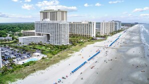 Un hôtel situé sur la côte, composé de plusieurs immeubles de grande hauteur, doté d’une plage de sable et d’un parking.