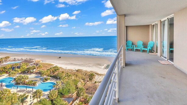 Un balcon avec des chaises turquoise, une piscine et une vue sur la plage et l’océan.