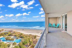 Un balcon avec des chaises turquoise, une piscine et une vue sur la plage et l’océan.