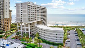 Un hôtel à plusieurs étages, doté d’une façade incurvée, d’un parking et offrant une vue sur la plage.