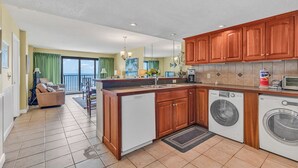 A kitchen with wooden cabinets, a dishwasher, a washing machine, and a dining area with a view.