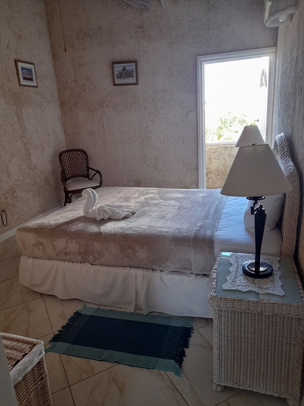 Un dormitorio con cama, una silla, una lámpara y vistas al exterior.