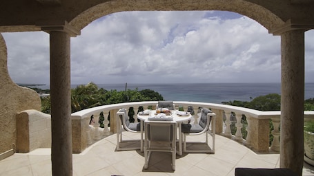 A balcony with a table set for dining, overlooking a scenic ocean view.