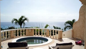 Ein Poolbereich mit Meerblick, ein bogenförmiger weißer Pool und eine Steinbalustrade.