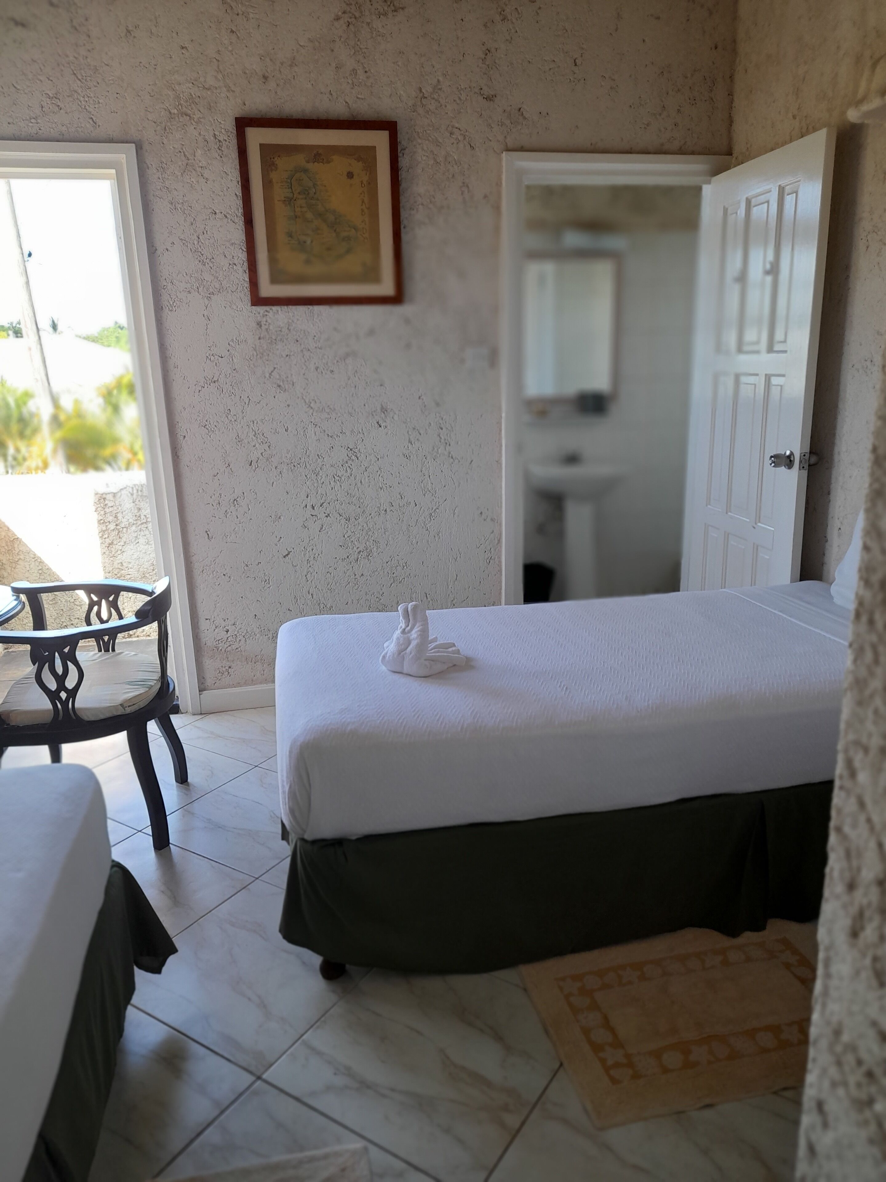 A hotel room with a bed, a chair, a small table, a door, and a wall-mounted picture.