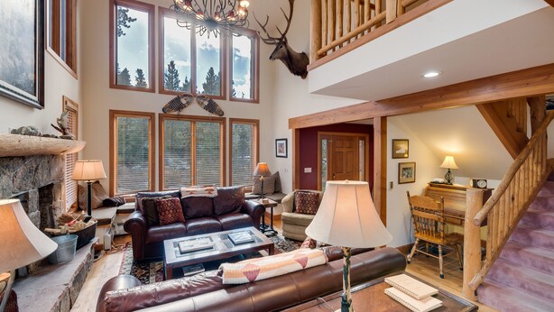 A spacious living room with a fireplace, leather sofas, a wooden staircase, and a deer head mounted on the wall.
