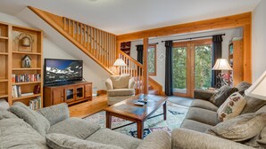 A cozy living room with a wooden staircase, a television, a sofa, and a bookshelf.