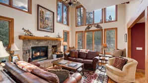 A spacious living room with a fireplace, leather sofas, and a large window offering a view of the outdoors.